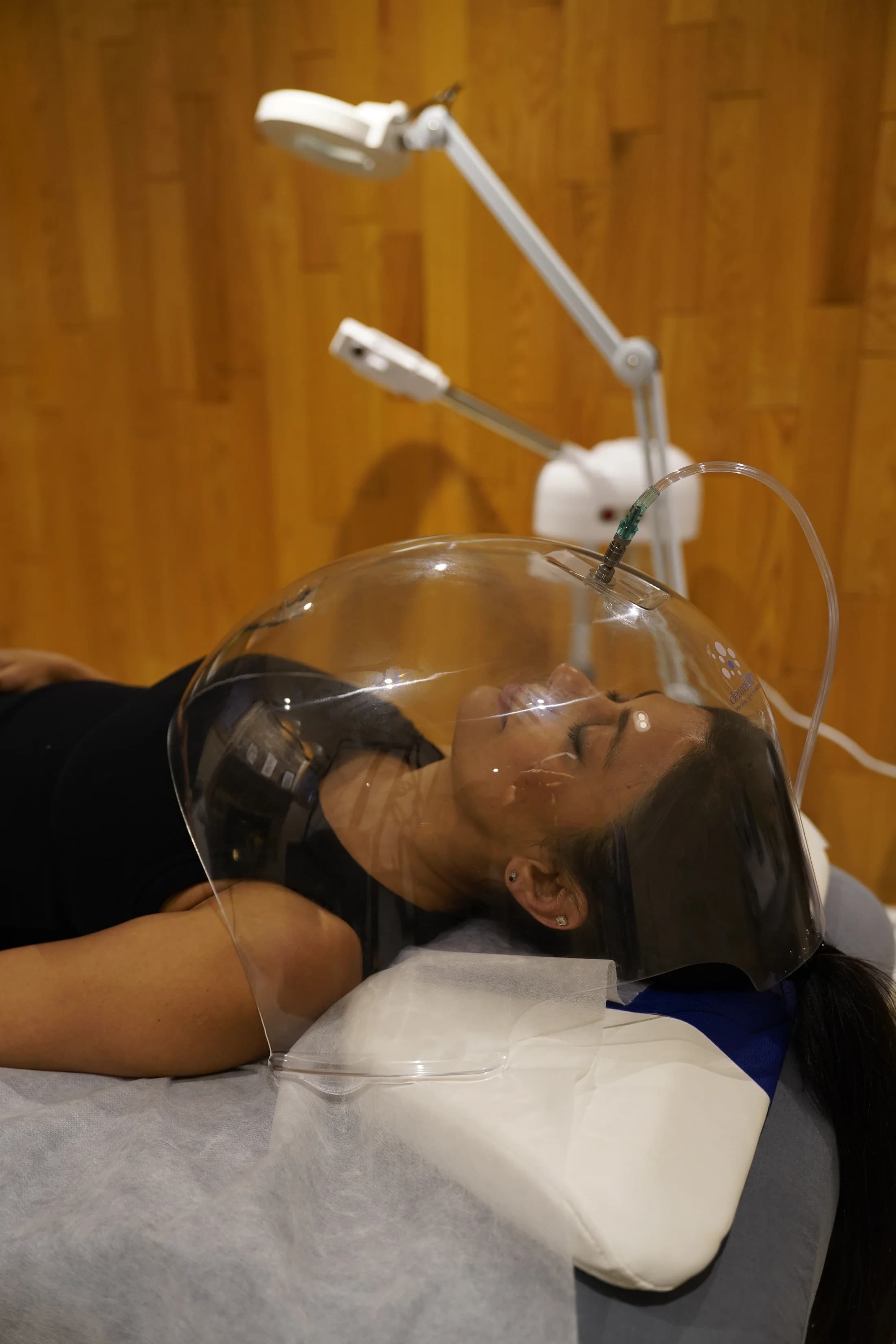 Client relaxing under the transparent oxygen dome during a facial treatment